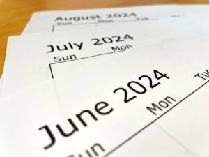 Three calendar pages for June, July and August are laid out on a table.